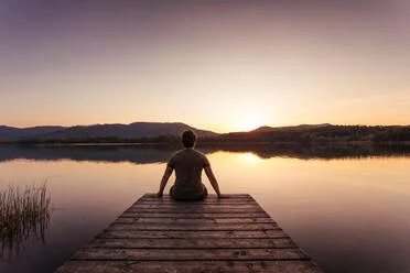 Mensch sitzt ruhig am See bei Sonnenaufgang – Symbol für Akzeptanz und inneren Frieden im Umgang mit Misophonie